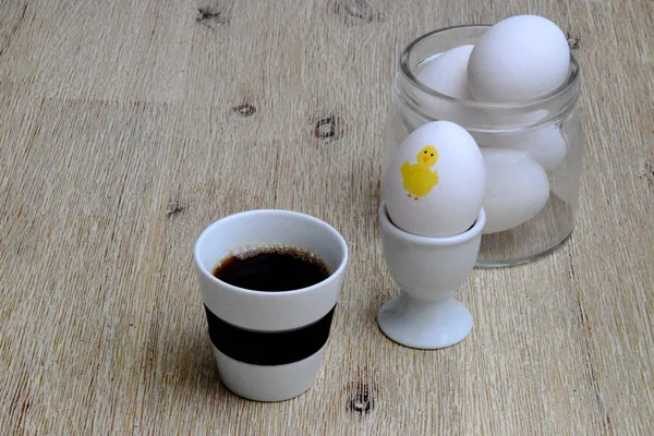 Coffee and eggs for breakfast this Easter! Photo of a cup of black coffee, glass bowl of eggs and a boiled egg in an egg cup, with a yellow Easter chicken painted on it.