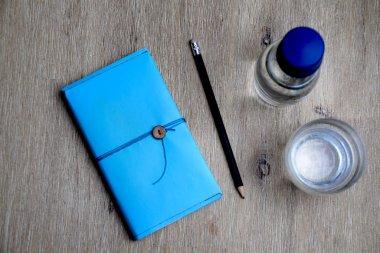 Mavi defter görünümünü, ahşap masa su ile kalem, cam ve cam şişe