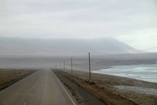 在雾蒙蒙的早晨 空旷的道路蜿蜒沿着海岸线蜿蜒前行 背景是山脉 泛美公路的道路部分和拍摄的照片就在秘鲁查拉港城外 — 图库照片