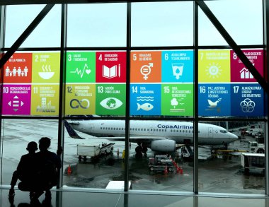 The Global Goals displayed in Spanish on the windows at Panama City Tocumen International Airport. Mother and child looking out to see the planes. Photo taken in Panama City/Panama, October 18, 2018. clipart