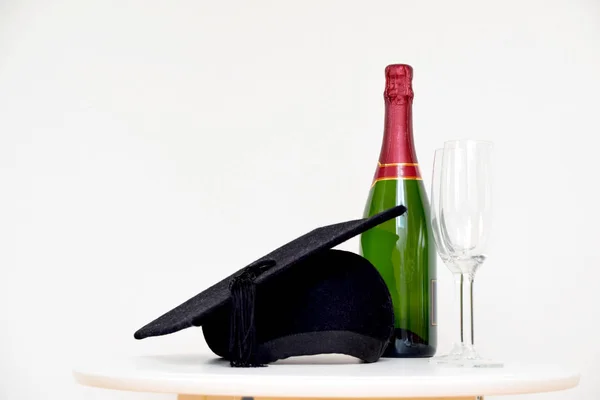 Graduation celebration with graduation cap, champagne bottle and glasses on white table