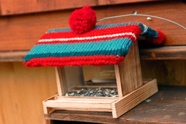 Wooden birdhouse carries a woolen jelly bag cap. Winter decoration. clipart