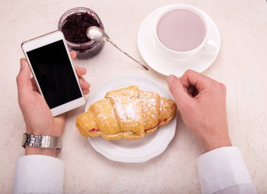 Kruvasan ile Ahududu reçeli, kakao el cep telefonu bir kupa. İş kahvaltı kavramı.