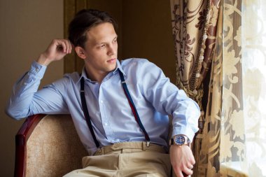 Damat pencereden dışarı bakarak, bekleyen koltukta oturuyor. Odaya.