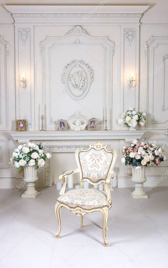 Luxury stylish bright light interior room. In the middle of the room chair. The white walls are decorated with ornaments. Fireplace. The flower vases bukety. Rich Baroque.