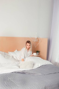 Yatak ve çay tadını çıkarırken bir dizüstü bilgisayar ile genç ve güzel kadın