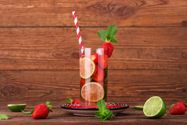 Fresh lemonade with strawberries, lime and mint in a tall glass on a wooden background