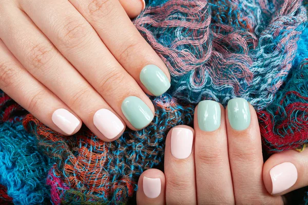 Hands with short manicured nails colored with pink and green nail polish