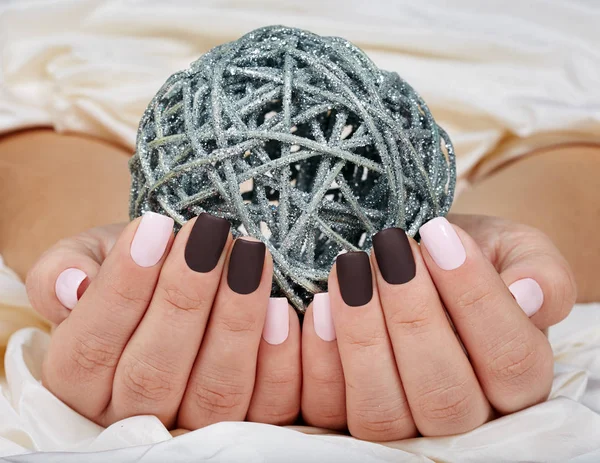 Hands with manicured nails colored with pink and purple nail polish holding a silver Christmas ball