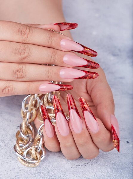Hands with long red artificial french manicured nails holding a chain necklace