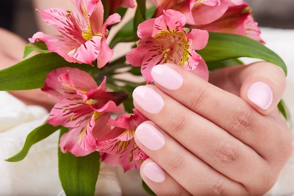 Hand with short manicured nails colored with pink nail polish and lily flowers