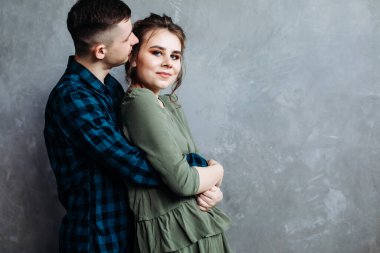 Yakışıklı bir adam kız arkadaşına arkadan sarılıyor. Mutlu Neşeli Aile. Sevgililer Günü. Gri bir duvara karşı poz vermek.