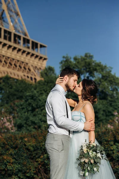 一对新郎新娘在巴黎的婚礼上 在埃菲尔铁塔的背景下 有一个浪漫的时刻 新娘手里拿着结婚花束 蓝色婚纱 — 图库照片
