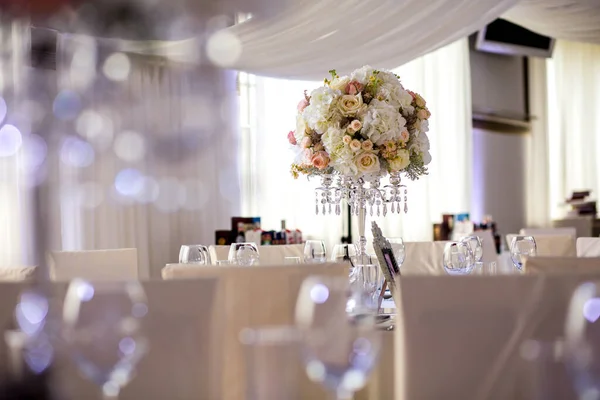 Large classical composition. from cream roses, white hydrangeas in a wedding composition in the form of a ball on a crystal chandelier. Stylish and luxuriously designed dining table for event guests.