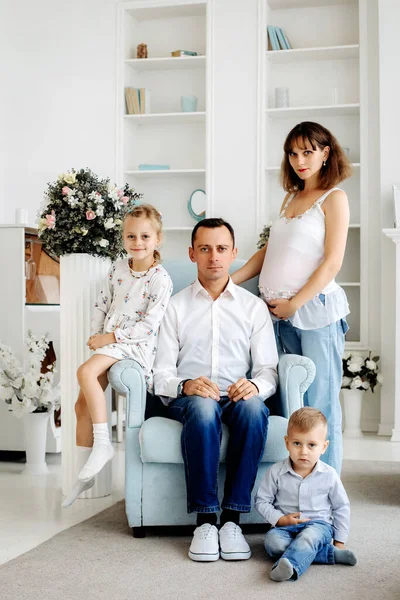 A large family waiting for their third child. a pregnant woman and a father with two older blond children . happy family life. Family photo in a light interior