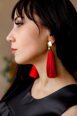 Temiz makyajlı, siyah saçlı ve kırmızı küpeli genç bir kadının yakın çekimi. Siyah ve kırmızı rengin kombinasyonu. .