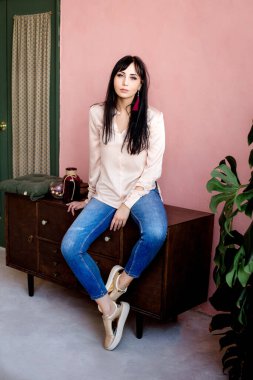 Genç bir Asyalı kız pembe beton bir duvara karşı komodinin üzerinde oturuyor..