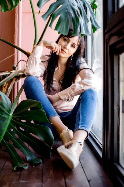 Sad Asian young woman brunette sitting on the window of the house alone, looking thoughtfully at the camera. Nostalgia — Stock Photo, Image