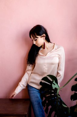 Kız, büyük bir çiçeğin yanında beton pembe bir duvara karşı duruyor ve evin içinde bir komodinin yanında. Metin için boşluk.