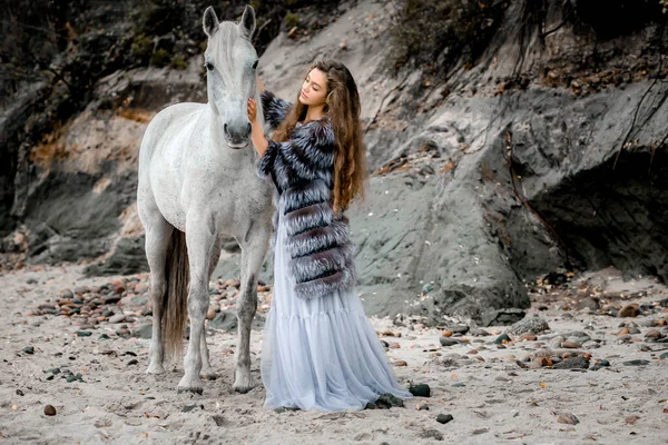 Una hermosa joven abraza a un caballo blanco. clima fresco, La amistad de la mujer y el animal. — Foto de Stock