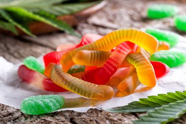 Cannabis infused gummy candy on a rustic table top with marijuana leaves. clipart