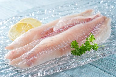 Fresh haddock fillets on glass plate with lemon and parsley. clipart