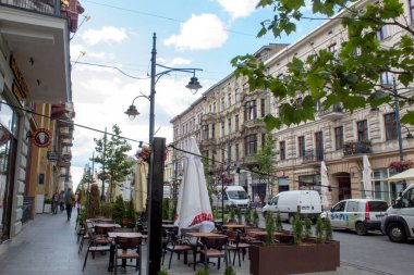 Lodz, Polonya - 09 Temmuz 2019: Yaz mevsiminin doruğunda Polonya'nın Lodz şehrinin merkezi tarihi caddesinde turistler için masa ve masalarla rahat kafeler.