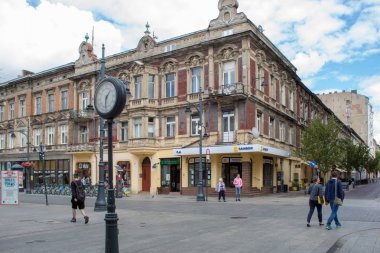 Lodz, Polonya - 09 Temmuz 2019: Güneşli bir yaz gününde Polonya'nın Lodz kentinin ana turistik caddesinde saat, turistler ve eski restore edilmiş mimari.