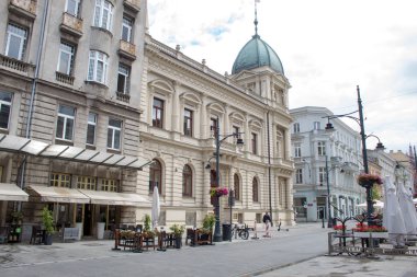 Lodz, Polonya - 09 Temmuz 2019: Yaz mevsiminin doruğunda Polonya'nın Lodz şehrinin merkezi tarihi caddesinde turistler için masa ve masalarla rahat kafeler.