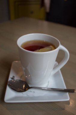 Siyah sıcak çay ve limon, beyaz porselen tabak, kahverengi bir masada bir çay kaşığı ile beyaz porselen fincan.