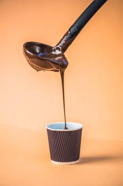 Bej renkli arka plan üzerinde kepçe ile kağıt bardak sıcak çikolata dökme
