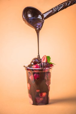 bej renkli arka plan üzerinde eritilmiş çikolata ile plastik kap içinde dökme taze çilek