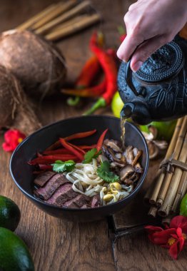 insan el Vietnamca Pho su dökerek ahşap masa üzerinde siyah kase çorba