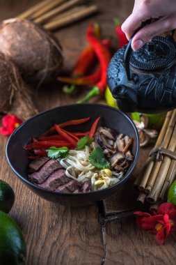 insan el Vietnamca Pho su dökerek ahşap masa üzerinde siyah kase çorba