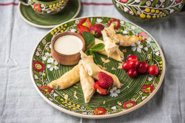 Taze çilek ve ekşi krem ile çiçek desenli plaka üzerinde tatlı haddelenmiş krep