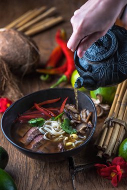 insan el Vietnamca Pho su dökerek ahşap masa üzerinde siyah kase çorba