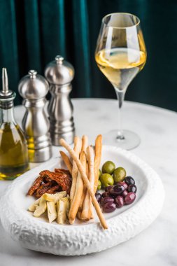 Siyah ve yeşil zeytin, enginar kurutulmuş domates ve peynir çubukları beyaz plaka üzerinde servis