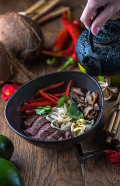 insan el Vietnamca Pho su dökerek ahşap masa üzerinde siyah kase çorba