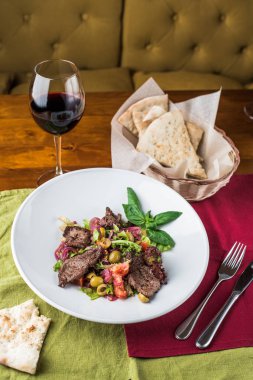 Masa örtüsü üzerinde kırmızı şarap bardağı ile kase et parçaları ile taze sebze salatası