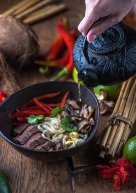 insan el Vietnamca Pho su dökerek ahşap masa üzerinde siyah kase çorba