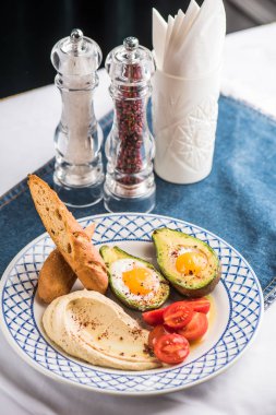 Avokado, domates, ekmek ve tabak üzerinde kızarmış yumurta ile ev yapımı humus