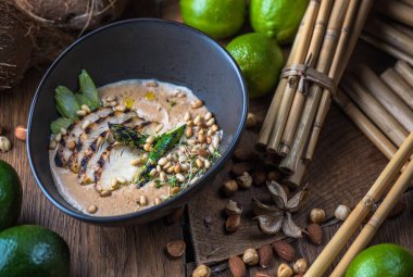 Tay çorba, et, fındık ve sebze malzemelerle ahşap masa üzerinde siyah kase krem