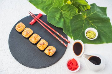 Japon Suşi roll kayrak üzerinde beyaz zemin üzerine yeşil yaprakları ile görev yaptı