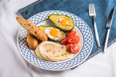 Avokado, domates, ekmek ve tabak üzerinde kızarmış yumurta ile ev yapımı humus