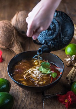 insan el Vietnamca Pho su dökerek ahşap masa üzerinde siyah kase çorba