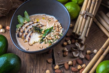 Tay çorba, et, fındık ve sebze malzemelerle ahşap masa üzerinde siyah kase krem