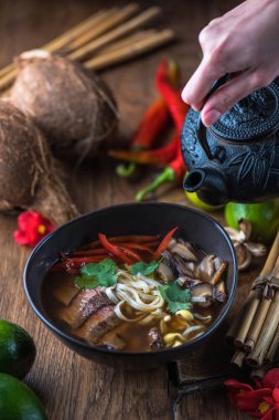 insan el Vietnamca Pho su dökerek ahşap masa üzerinde siyah kase çorba