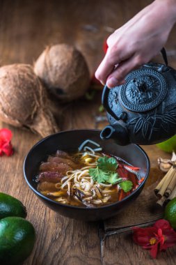 insan el Vietnamca Pho su dökerek ahşap masa üzerinde siyah kase çorba