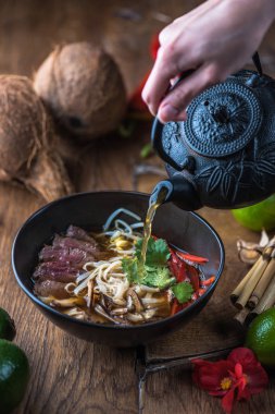 insan el Vietnamca Pho su dökerek ahşap masa üzerinde siyah kase çorba