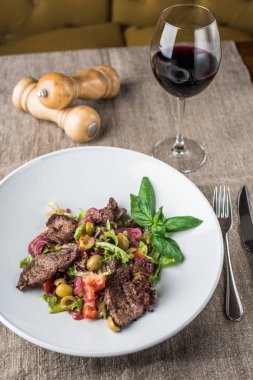 Masa örtüsü üzerinde kırmızı şarap bardağı ile kase et parçaları ile taze sebze salatası